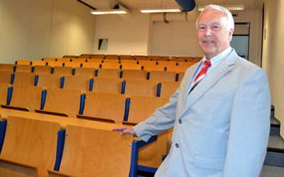 Ein Mann in grauen Anzug und mit roter Krawatte steht in einem Hörsaal.