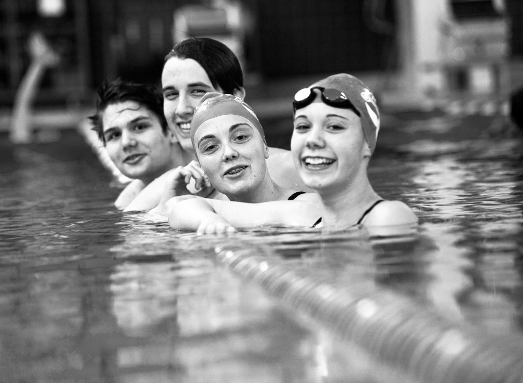 Zwei junge Männer und zwei junge Frauen in einem Schwimmbecken lächen in die Kamera.