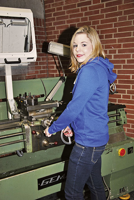 Eine blonde junge Frau in blauem Pulli an schwerem Gerät.