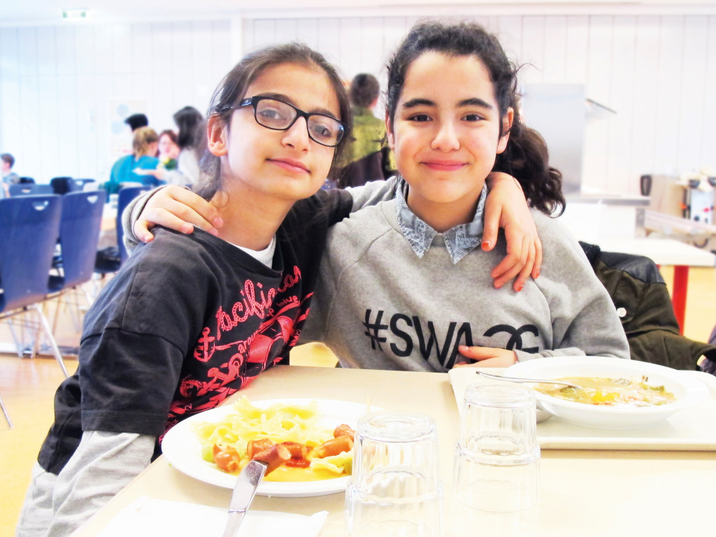 Zwei Schülerinnen lächeln beim Essen in die Kamera.