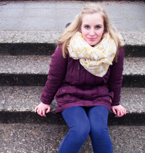 Eine blonde Schülerin sitzt auf einer Treppe und lächelt in die Kamera. 