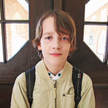 Ein Schüler in heller Jacke steht vor einer Holztür.