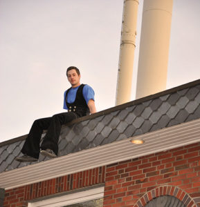 Ein junger Mann in Arbeitskleidung sitzt auf einem Dach.