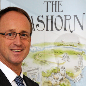 Ein Mann im Anzug steht lächelnd vor einem Poster.