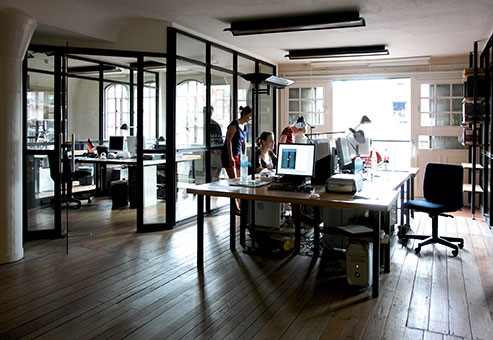 Ein Büro mit Holzböden. Menschen arbeiten mit Computern. Diese stehen auf Schreibtischen