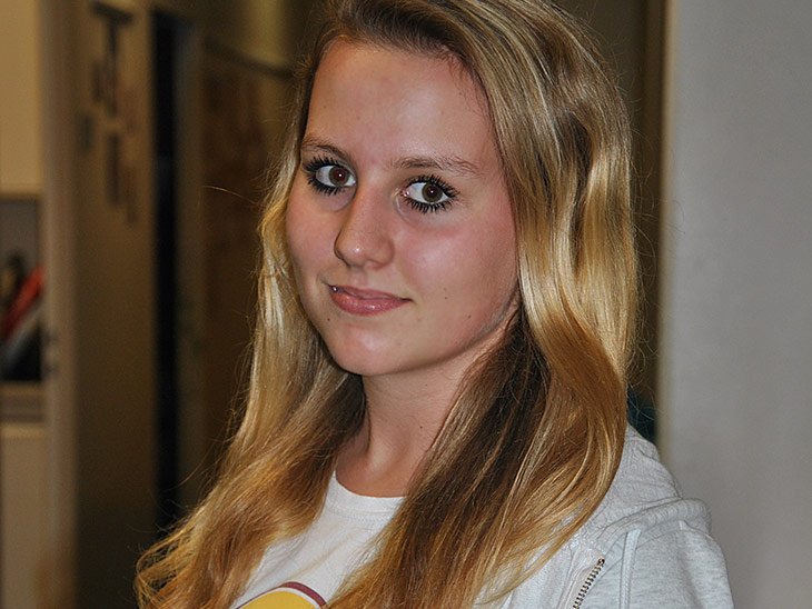 Eine blonde Schülerin mit braunen Augen lächelt in die Kamera.