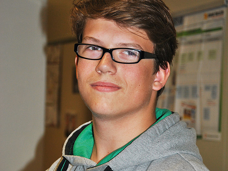 Ein Schüler mit Brille lächelt in die Kamera.