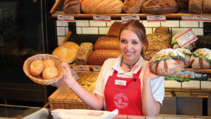 Eine junge Frau steht in einer Bäckerei und lächelt in die Kamera.