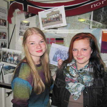 Zwei Schülerinnen stehen vor einer Wand mit Fotos.