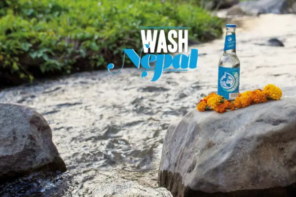 Eine Flasche steht auf einem Felsen in einem Fluß. Ein Schriftzug mit „Vivia con agua" befindet sich daneben."