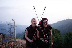 Zwei junge Frauen in Wanderausrüstung stehen auf einem Berg und lachen. 