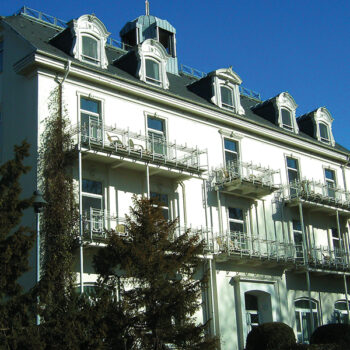 Ein dreistöckiges Haus mit heller Fassade unter blauem Himmel.