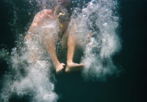 Ein Mensch springt ins Wasser. Um ihn herum wirbeln Luftblasen. 