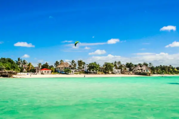 Ein Strand mit türkisem Wasser. Am Himmel fliegen Kite-Schirme.