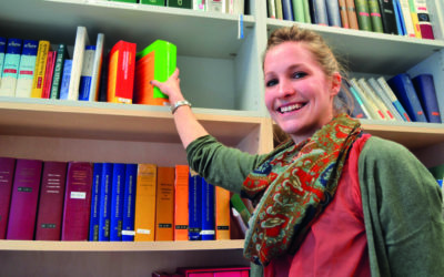Eine blonde junge Frau greift in ein Bücherregal.