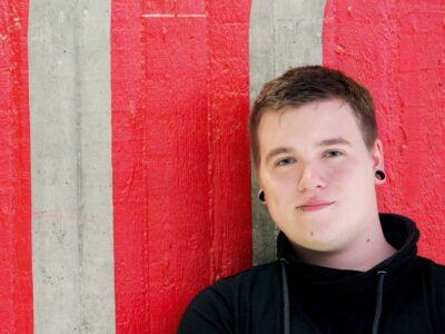 Ein junger Mann vor einer rot-weißen Wand.