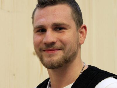 Ein junger Mann steht vor einer Holzwand.