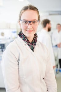 Eine junge Frau in weißer Schutzkleidung lächelt in die Kamera. 