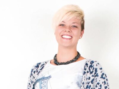 Eine junge blonde Frau mit halblangen Haaren lächelt in die Kamera.