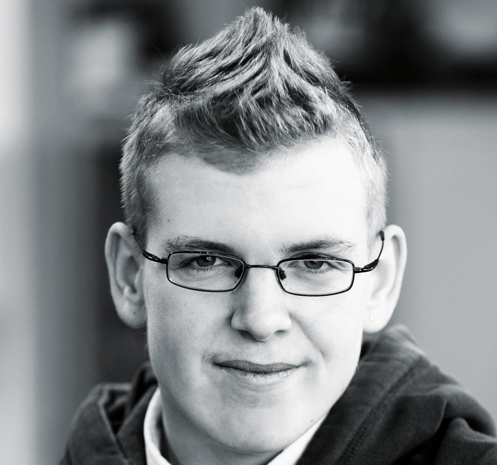 Ein blonder junger Mann mit Brille und gegelten Haaren.