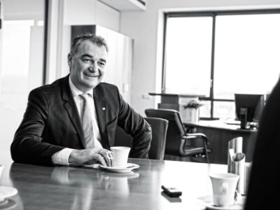 Ein Mann im Jackett sitzt einem anderen Mann an einem Holztisch gegenüber.
