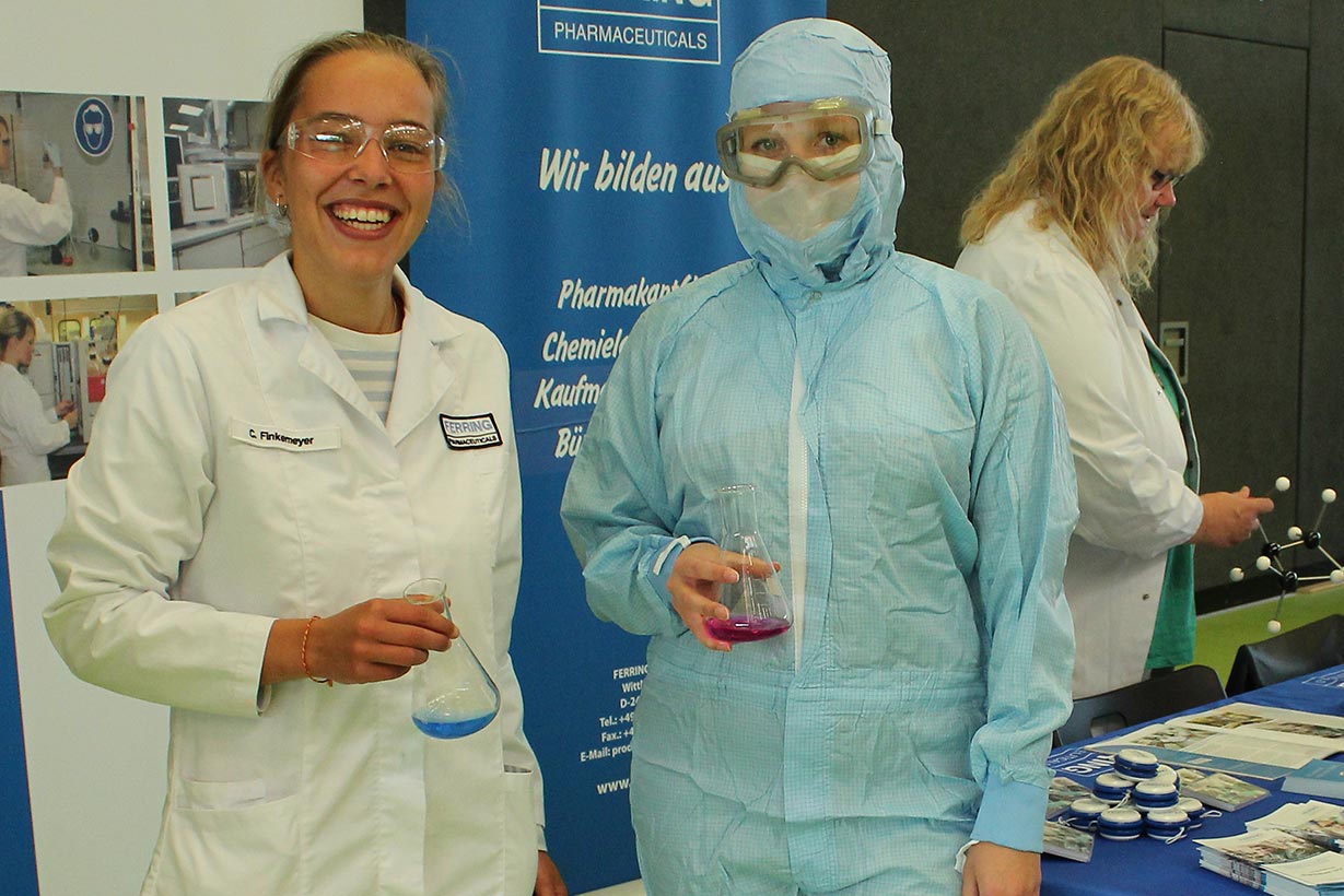 Ein Mädchen im Laborkittel lacht und ein Mädchen im Sterilanzug steht daneben.