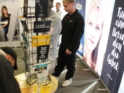Ein junger Mann in einem schwarzen Overall steht an einem Stand.