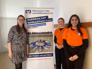 drei Personen stehen vor einem Plakat der Dithmarscher Volks- und Raiffeisenbank 
