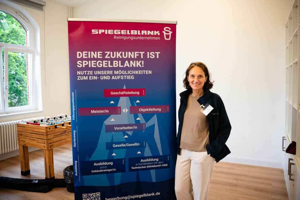 Eine dunkelhaarige Frau steht vor einem Rollup der Firma Spiegelblank aus Kiel. 