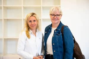 Zwei Frauen stehen nebeneinander und lächeln in die Kamera.