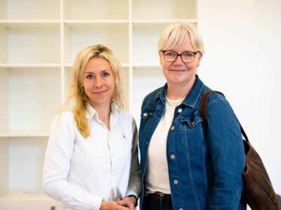 Zwei Frauen stehen nebeneinander und lächeln in die Kamera.